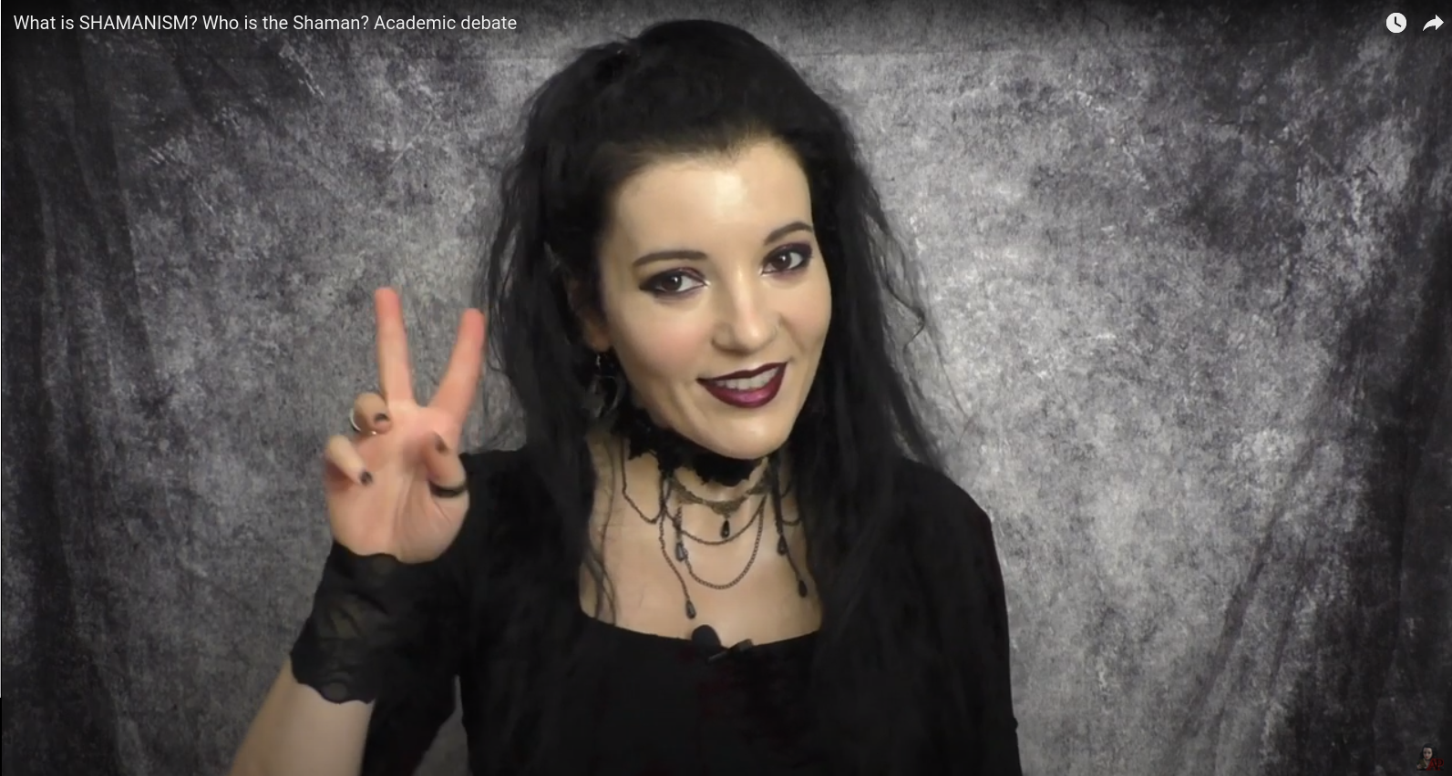 Angela Puca in black with a choker holding two fingers to indicate two