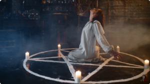 Woman kneeling on a pentagram with lit candles on each point